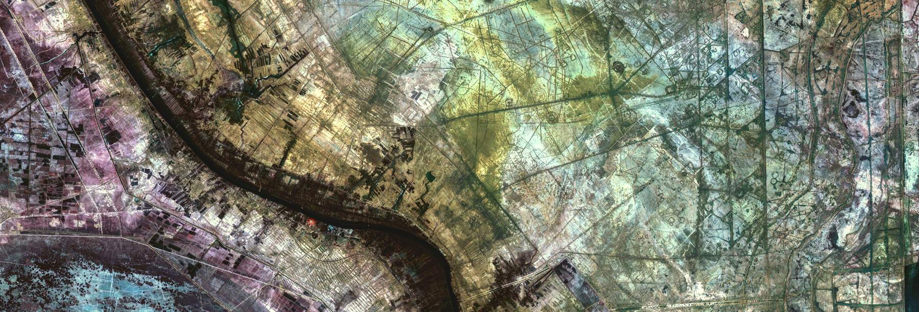 False-color aerial image of a river cutting through layered sedimentary terrain.
