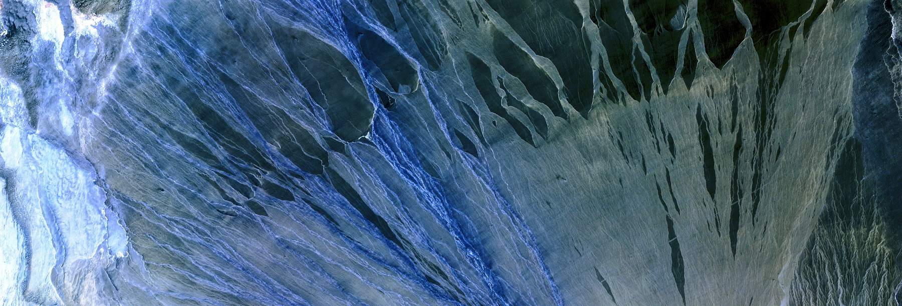 False-color aerial image of an alluvial fan spreading across pale terrain.