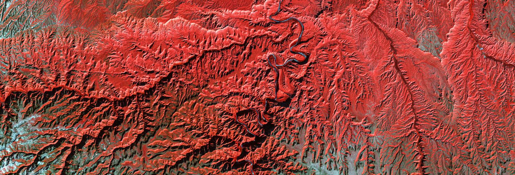 False-color aerial image of a mountain range rendered in deep red.