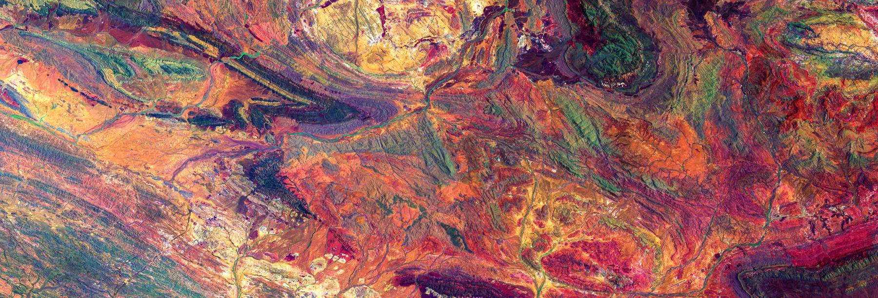 False-color aerial image of folded rock strata in red and ochre.