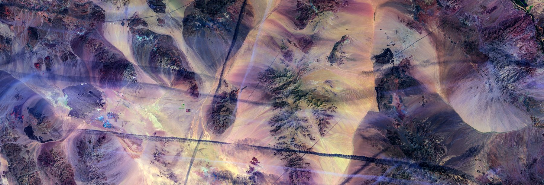 False-color aerial image of desert dunes in muted violet and grey.