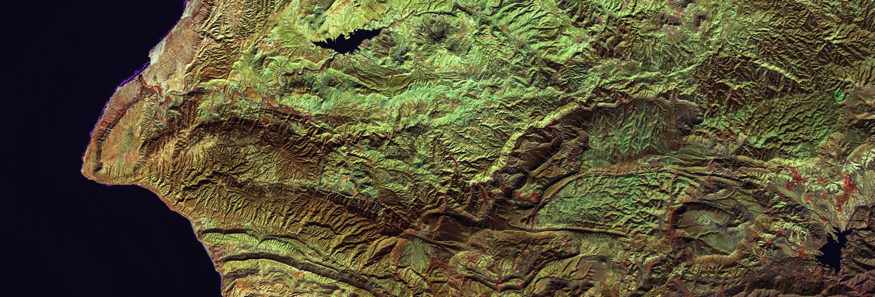 False-color aerial image of an escarpment against deep shadow.